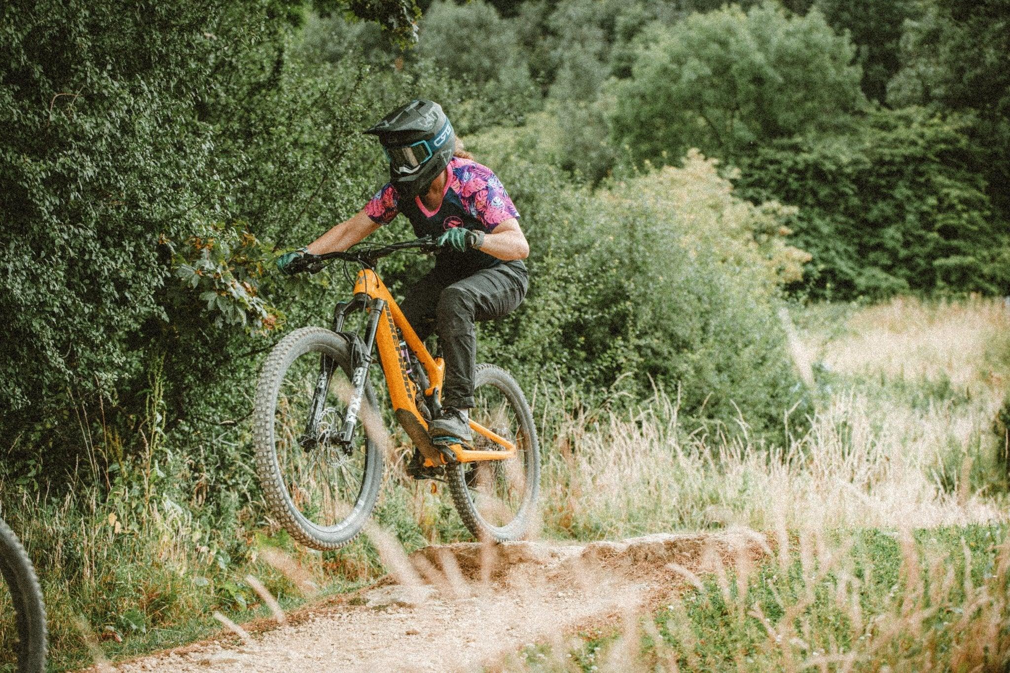 Mountain biker in pink and black MTB jersey and helmet jumping orange mountain bike on forest trail