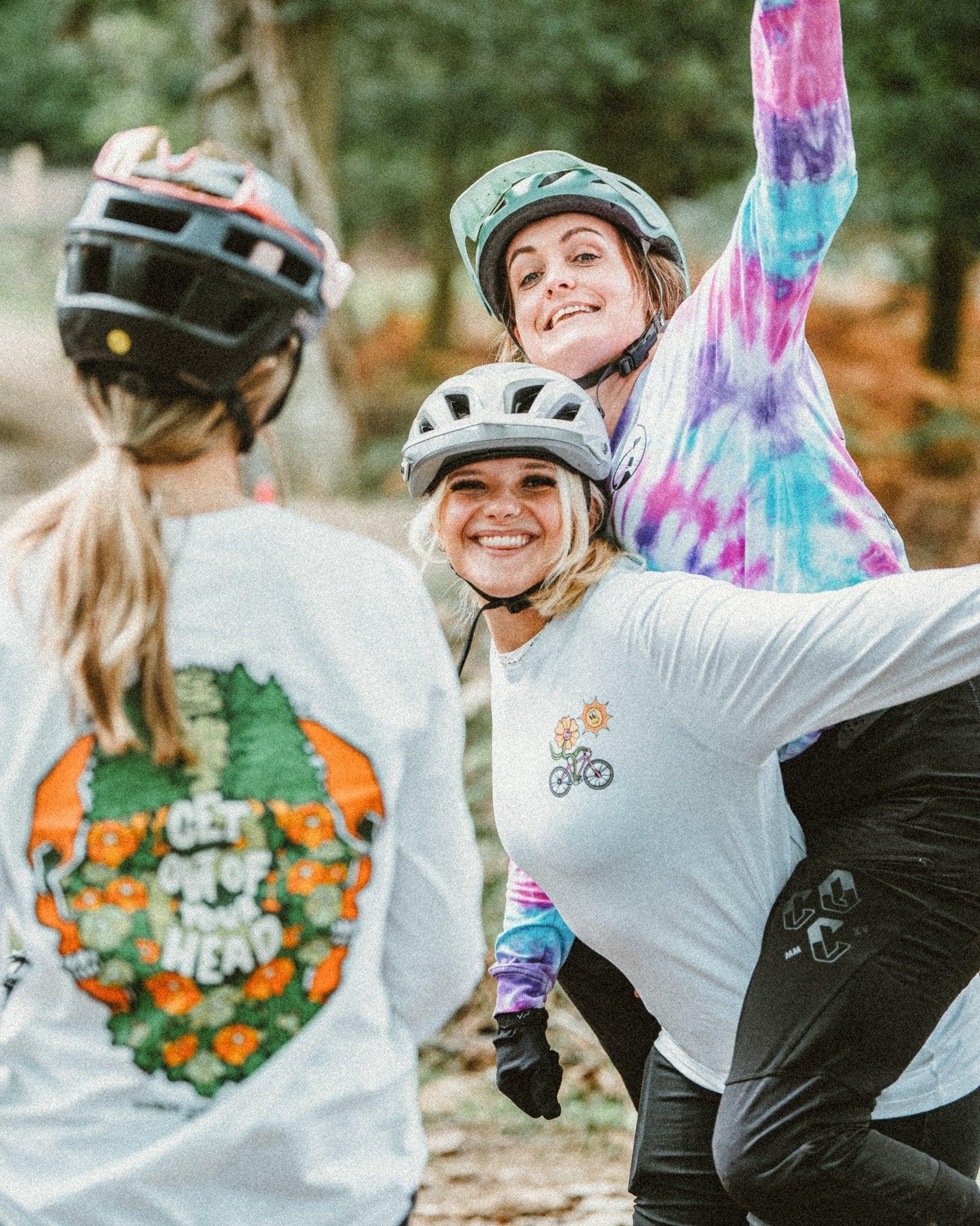 Three women outdoors wearing sustainable mountain bike helmets and colorful MTB apparel with nature graphics, smiling and enjoying