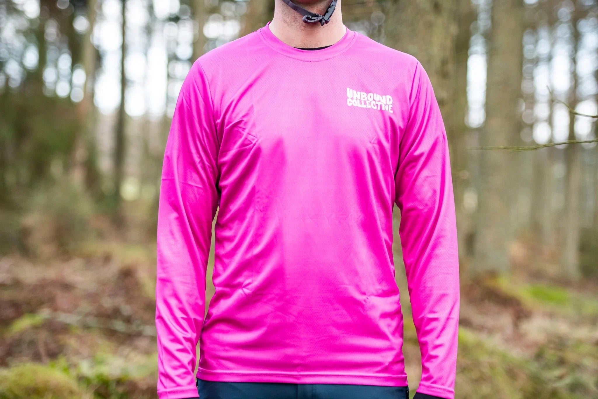Man wearing bright pink long-sleeve Unbound Collective mountain bike jersey in forest setting