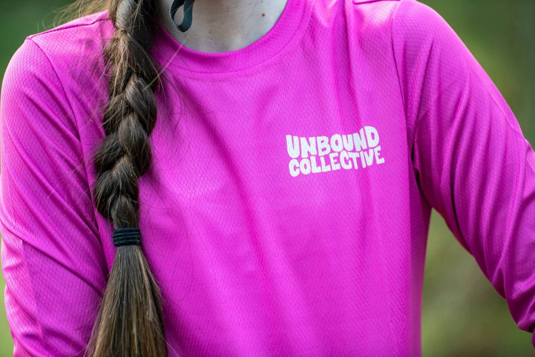 Close-up of woman wearing bright pink Unbound Collective mountain bike jersey with long braid