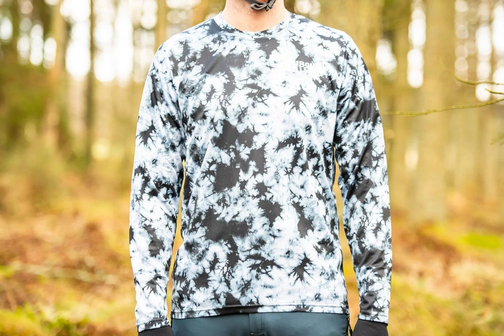 Man wearing black and white smoke patterned long-sleeve mountain bike jersey outdoors in forest
