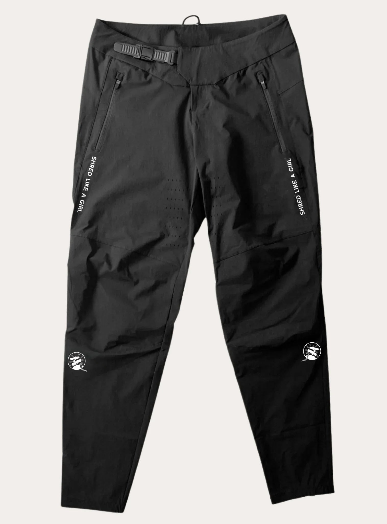 Black women's mountain bike trail pants with zippered pockets, belt buckle, and white "Shred Like A Girl" text