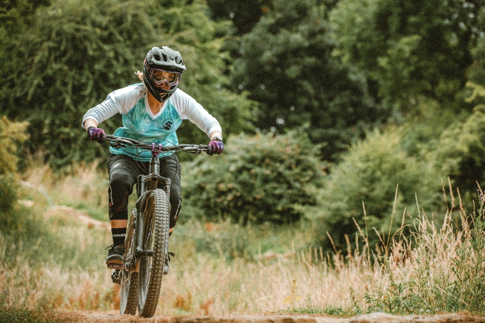 Mountain biker wearing helmet and protective gear riding on a forest trail surrounded by greenery