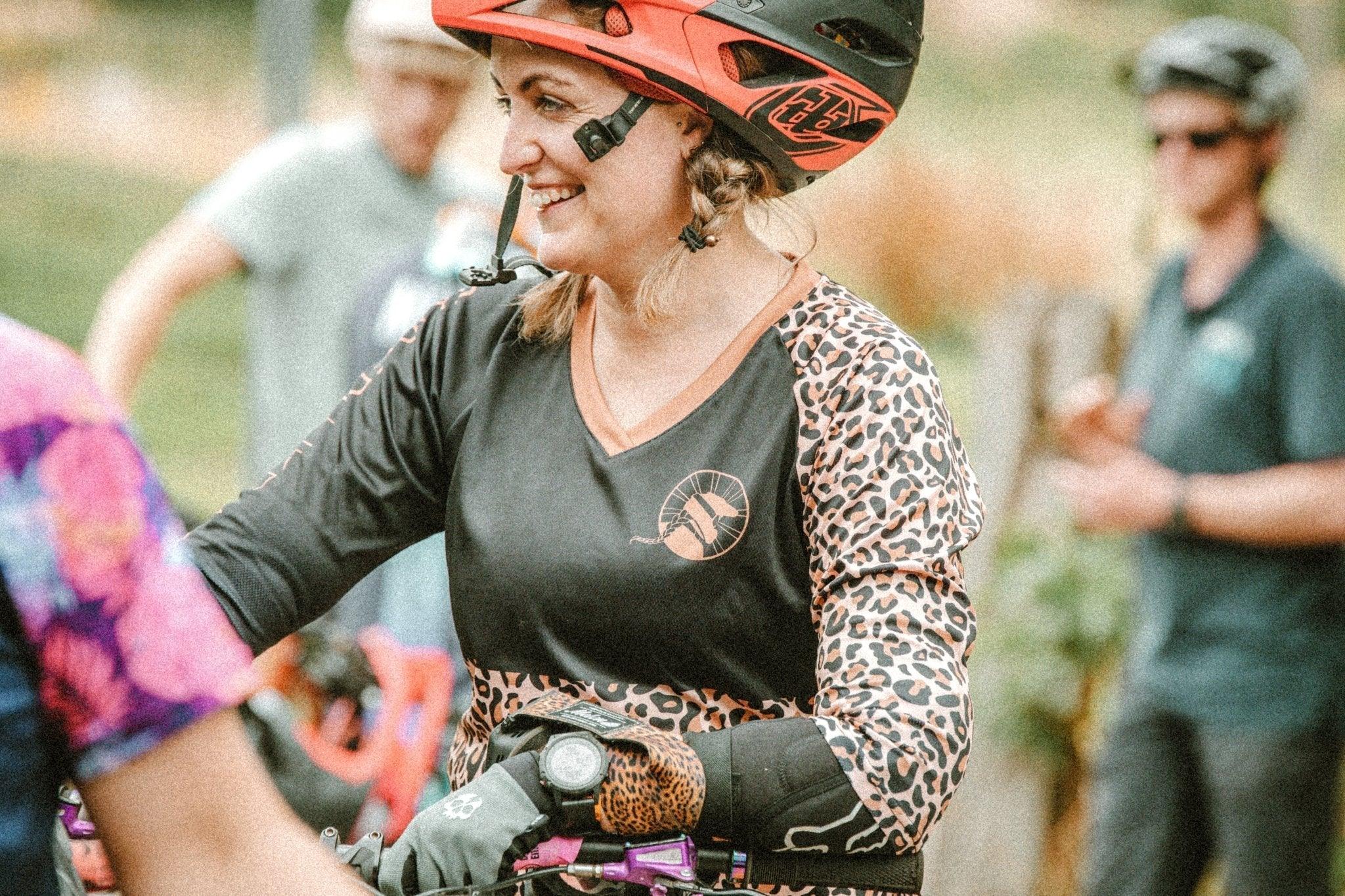 Smiling woman wearing leopard print MTB jersey and red helmet at outdoor biking event