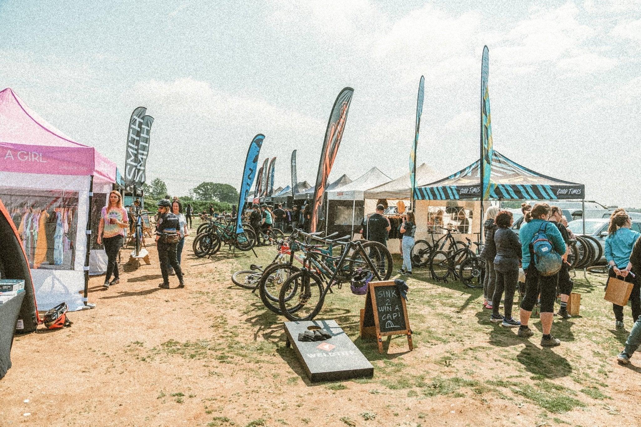 Outdoor mountain bike festival with tents, bike displays, brand flags, and attendees browsing MTB gear