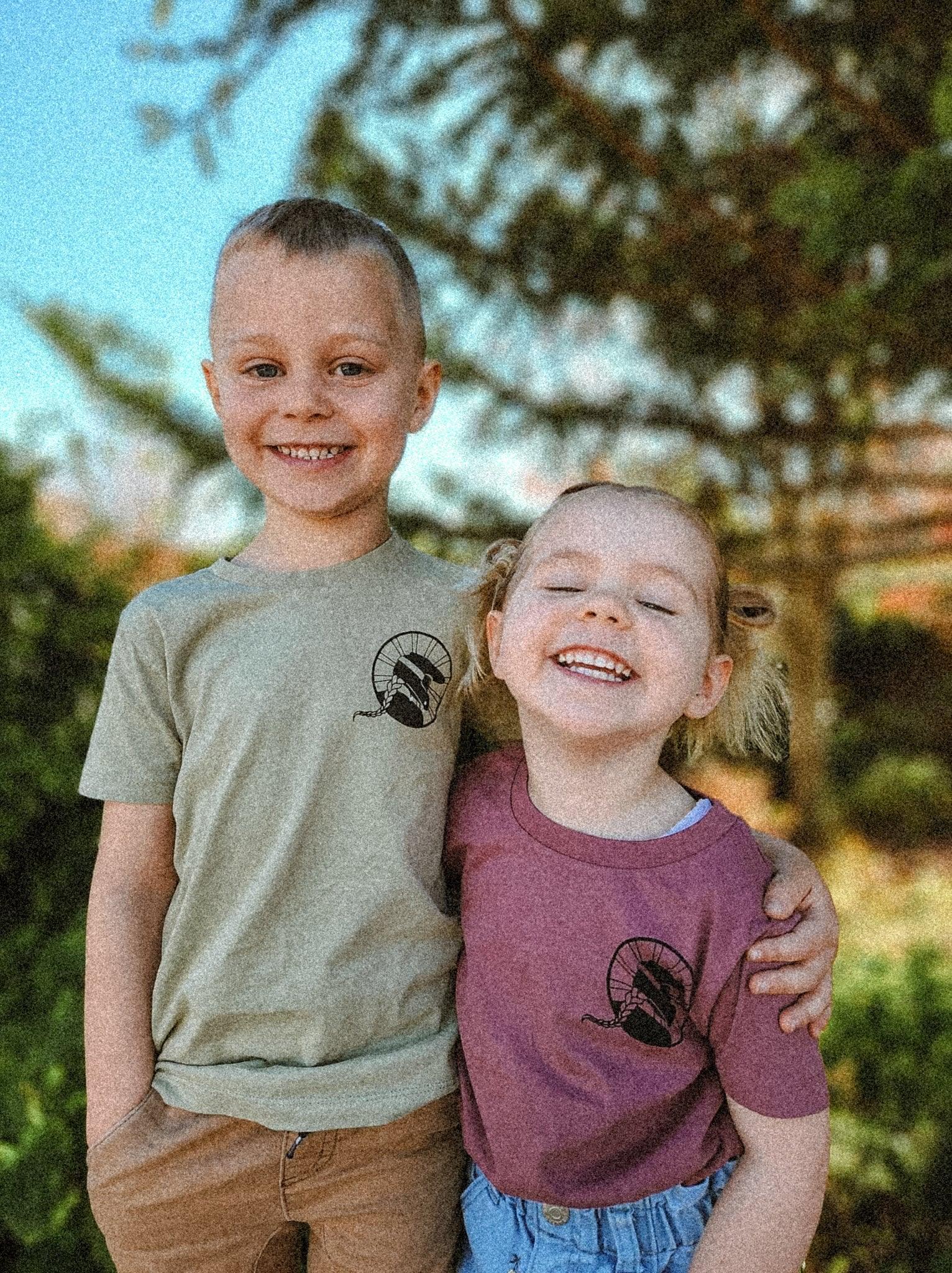 Smiling boy and girl wearing sustainable mountain bike apparel tees with graphic logos outdoors
