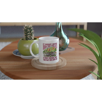 White ceramic mug with colorful motivational cycling design on wooden table with green potted cactus and glass vase